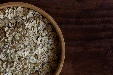 Oat flakes or oatmeals in wood bowl put on rustic wood table. Rolled oat is clean food for health lover people. Prepare oat flakes for bakery or cooking. Natural organic food in vintage style concept.