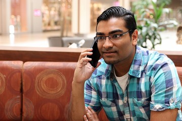 Young handsome man sitting on sofa talking on cell phone while wearing blue plaid shirt