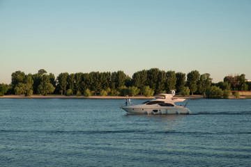 Obraz premium white boat with people sailing on the blue waters of the river on the background of green forest