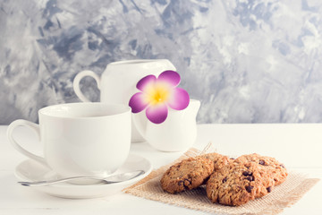 cup of coffee,milk,sugar,chocolate chip cookies and flower on white wooden background with loft wall style with light in concept relax time