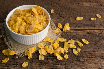 white bowl of cornflakes on sackcloth  on wooden background with copy space ,still life , in concept breakfast