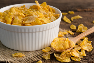 white bowl of cornflakes on sackcloth with wooden spoon on wooden background ,still life , in concept breakfas