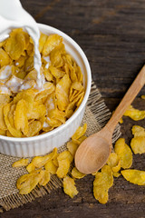 close up pour milk into white bowl of cornflakes on sackcloth   with wooden spoon on wooden background with copy space ,still life , in concept breakfast