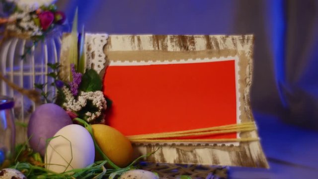a Photo Frame is Put Near a White Top Egg Cage, Rosy Tulips, a Bottle With a Lit Candle and Easter Hen and Quail Eggs, Laid Out on a Round Table