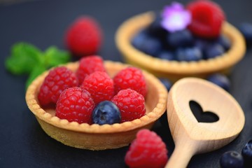 Törtchen mit Himbeeren und Heidelbeeren neben Holzlöffel Herz