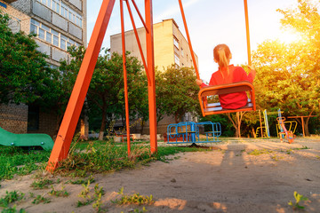 Little girl is riding on a swing in city house yard.