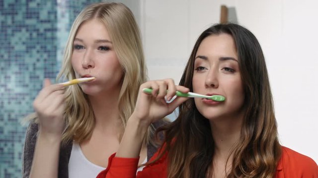 Two young women brushing teeth together infront of the camera