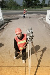 Surveyor or Engineer making measure by Theodolite with partner on the field.