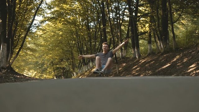 Hipster boy having fun riding siting on skateboards in park trees tunnel, 120FPS slowmotion