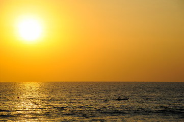 Tiny kayak boat silhouette at sunset