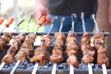 On the barbecue, a lot of meat is roasted on skewers, the chef turns over his shish kebabs. A man's hand turns, fries tasty meat of pork on skewers in Camping