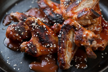 Closeup of grilled chicken wings served with tomato sauce and sesame seeds, selective focus, shallow depth of field
