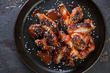Barbecued chicken wings served with sauce and sesame on a metal plate, flat-lay, horizontal shot