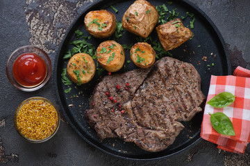 Above view of grilled ribeye beefsteak with baked potato on a metal plate, studio shot