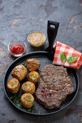 Frying pan with barbecued ribeye steak and baked potato, vertical shot on a brown stone background, selective focus