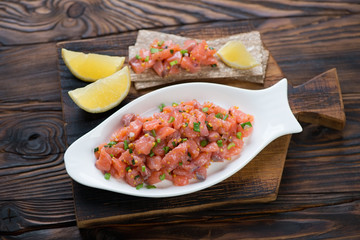 White plate with salmon tartare in a rustic wooden setting, horizontal shot