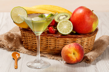 Kiwi jelly with lime pieces in the glass, fresh strawberries, nectarine, lime, kiwi, banana, apple in a wicker basket on the table