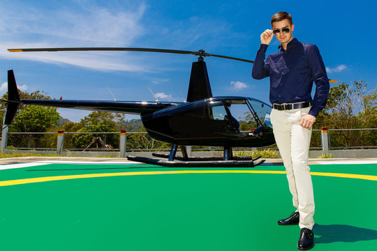 Young elegant man wearing sunglasses standing next to a private helicopter.