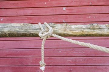Rope tied in a knot on a hitching post in front of a red barn wall