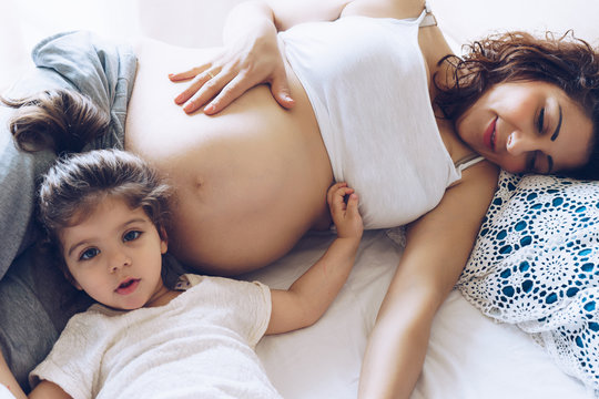 Beautiful pregnant woman and her cute little daughter together in bed