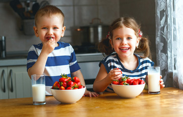 Happy children brother and sister eating strawberries with milk