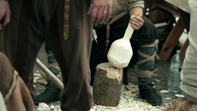 Carpenter in traditional costume hews wooden bailer with a hatchet