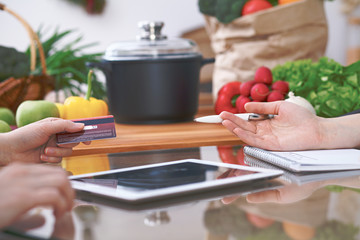 Close-up of four human hands are gesticulate over a tablet in the kitchen. Friends having fun while choosing menu or making online shopping. So much ideas for tasty cooking. 