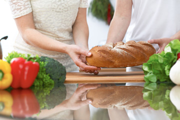 Close-up of human hands slicing bread in a kitchen. Friends having fun while preparing fresh salad. Chef cook represent culinary masterclass. Vegetarian, healthy meal and friendship concept