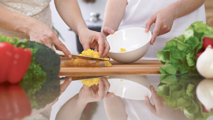 Close-up of four human hands are cooking in a kitchen. Friends having fun while preparing fresh salad. Vegetarian, healthy meal and friendship concept