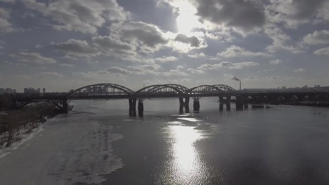 Aerial view on the city with river in cloudy weather. Modern bridge in spring season. On the coat unmelted snow. Industrial cityscape.