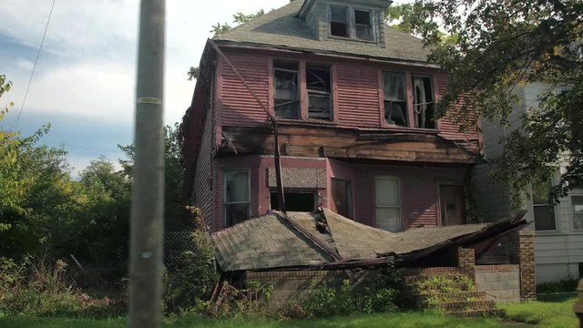 CLOSE UP: Driving past abandoned homes in poor neighborhood of Detroit, USA. Spooky empty haunted house with collapsed roof crumbling into pieces. Derelict crumbling ruined mansion in sunny suburbs