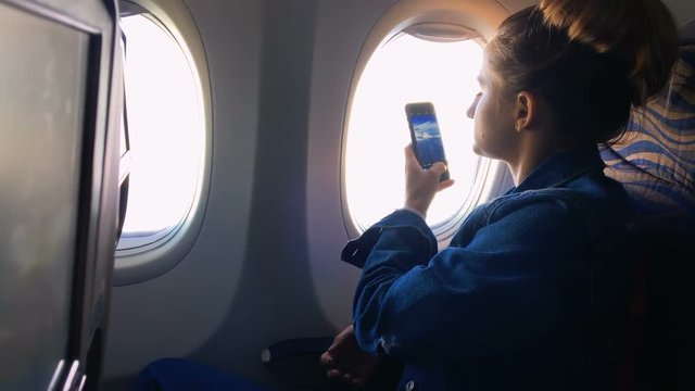 The girl climbs into the porthole and takes pictures of the landscape in the window on the phone. A young girl is traveling by plane. Slow motion 1080p