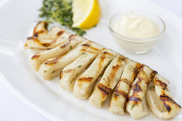 Whole grilled calamari in white plate, at restaurant, close-up, macro