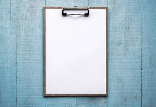 Clipboard with white sheet on wood background. Top view.Vintage style.