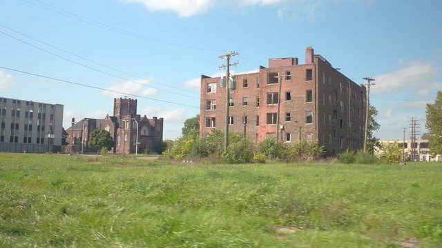 FPV Driving past huge brick-built residential building in ruins in decaying industrial zone of Detroit city, USA. Crumbling relict apartment block with broken windows near beautiful historic cathedral