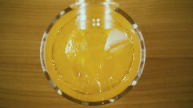 Completely fill a glass from a bottle with an orange drink and ice and orange top view. Slow mo