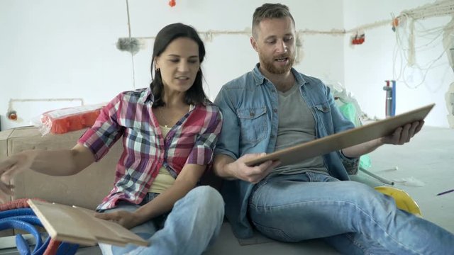 Young couple talking and choosing panels for new home sitting on floor
