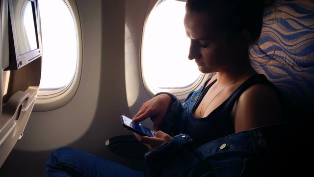 A young girl flies in an airplane and looks through photos from a vacation in a smartphone. 1080p