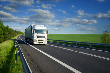 Fototapeta na wymiar White truck driving on the asphalt road along the green fields and alleys in the countryside