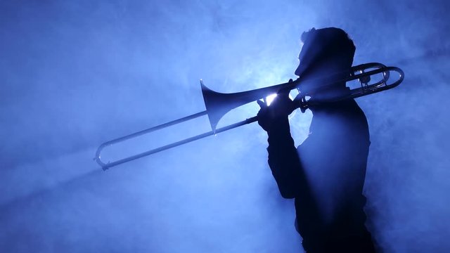 Trumpeter man in spotlight in smoky studio plays on trombone