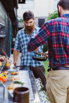 Two Men Cooking Outdoors At Barbecue Station Having Fun