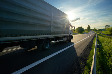 Truck driving against the glowing sun on an asphalt road in rural countryside