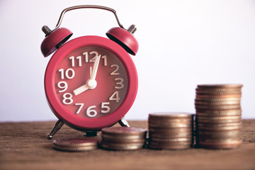 Row of coins and red alarm clock on wood background for finance and Saving concept,Investment, Economy, Soft focus and dark style.