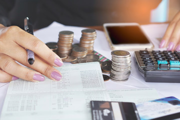 business woman hand analyzing on account book, with pile of coins , credit card and smart phone background