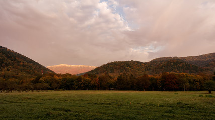 Autumn landscape at dawn with cloudy sky, meadow, mountain peak in the sunlight and forest. Caucasus. Russia. The Caucasian reserve. Cordon Guzeripl