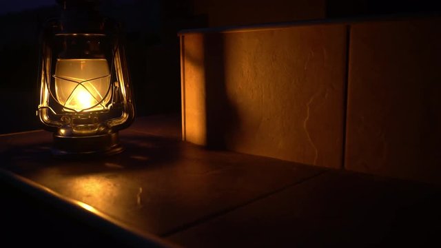 An ancient kerosene lamp stands on the steps of the house lit with a soft yellow light, in the street the night