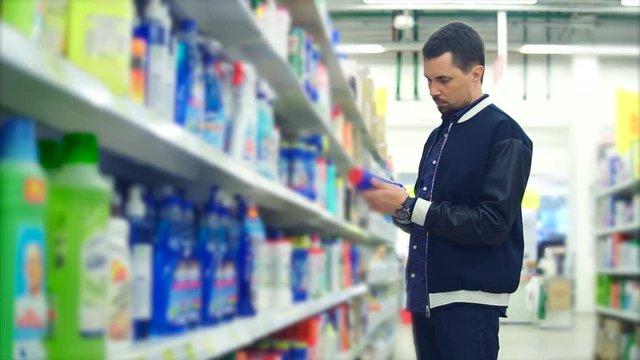 A middle-aged man chooses a means with bleach to clean his apartment, on the shelves in the giermarket there is a lot of goods for cleaning the bathroom, people are holding a blue jar