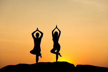 Silhouette of attractive confident half naked man and woman doing yoga on beach rock