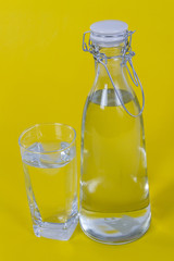 Bottled water and glass on yellow background