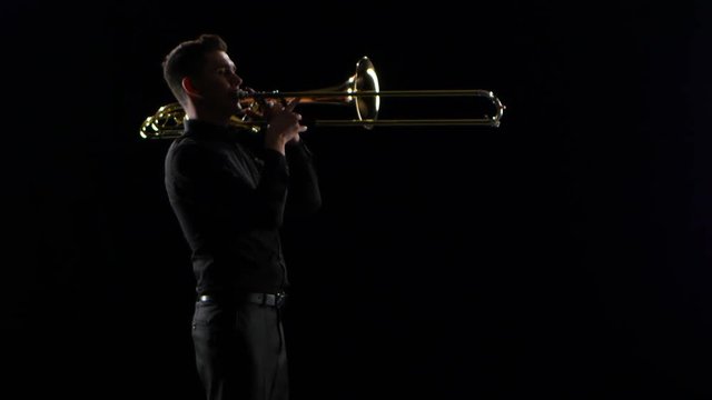 Trumpeter plays on wind instrument tranquil melody. Black studio background